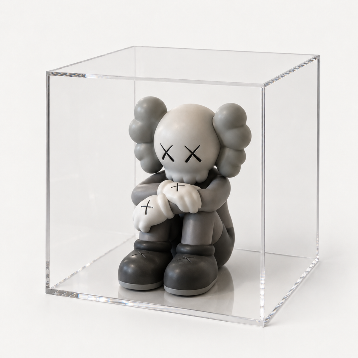 Grijs figuurtje met kruisvormige ogen in een transparante acryl vitrine.