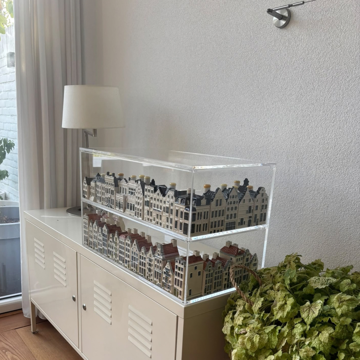 Twee lagen KLM-huisjes in transparante vitrines op een witte kast.